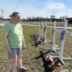 Collage artist Aleta Stone visits the white crosses put up in remembrance of those who died in the 2025 tornado. It's close to where she collected remnants for the collages that became art awards.
