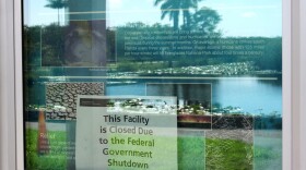 A sign alerting visitors that the Royal Palm Visitor Center is closed due to the federal government shutdown hangs in a display case reflecting the landscape, inside Florida's Everglades National Park, Wednesday, Oct. 1, 2025.  