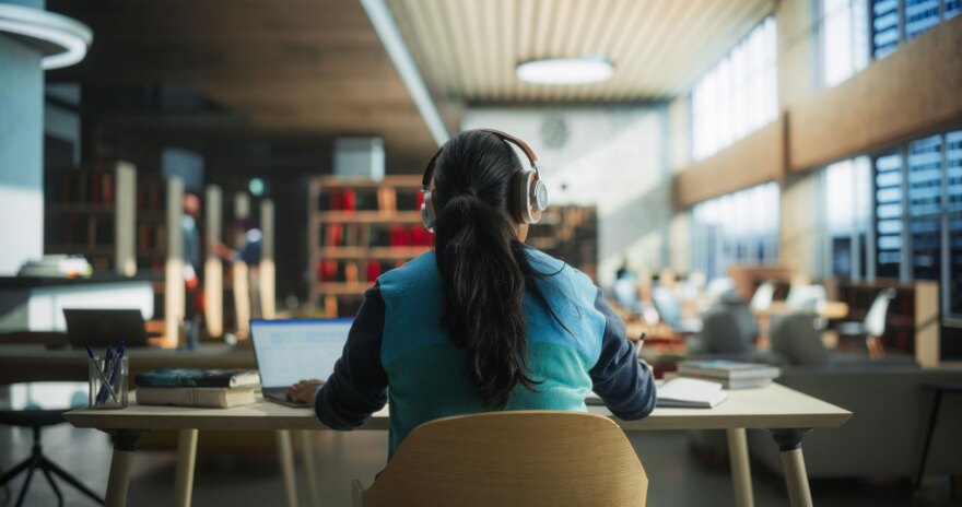 A student wearing headphones while working at a Library. Image for illustrative purposes only. The subject is a model. (Credit: Gorodenkoff/Adobe Stock)