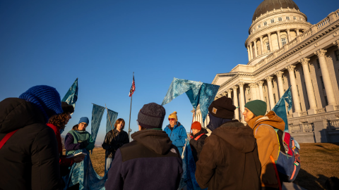 A crowd is gathered outside the Utah Capitol building holding flags that resemble water