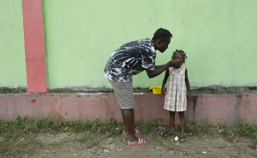A father cleans his daughter's face at the soccer stadium in Les Cayes on Thursday. The night before, a thunderstorm and an aftershock rattled people staying in the soccer stadium.