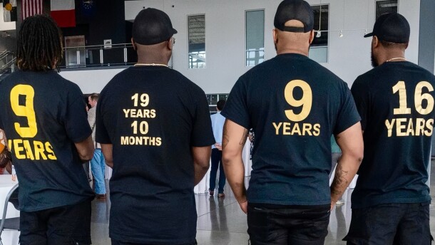 Members of the Organization of Exonerees wear t-shirts displaying the exact number of years they spent wrongfully incarcerated for crimes they did not commit. All the t-shorts are black and the numbers are on the back. The far left on says 9 years. The one next to it says 19 years and 10 months. The next one also says 9 years and the last says 16 years. 