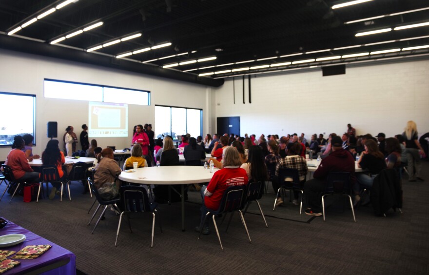 A crowded conference room, full of elected officials and community leaders at the Douglass Community Association, watches students present solutions for gun violence.  A table with food can be seen in the lower left corner of the frame.