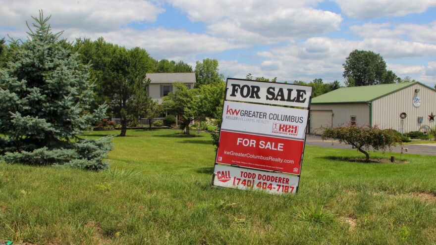 A sign in front of a rural home reads "FOR SALE: KW Greater Columbus / FOR SALE kwGreaterCoumbusRealty.com / call Todd Dodderer (740) 404) 7187"