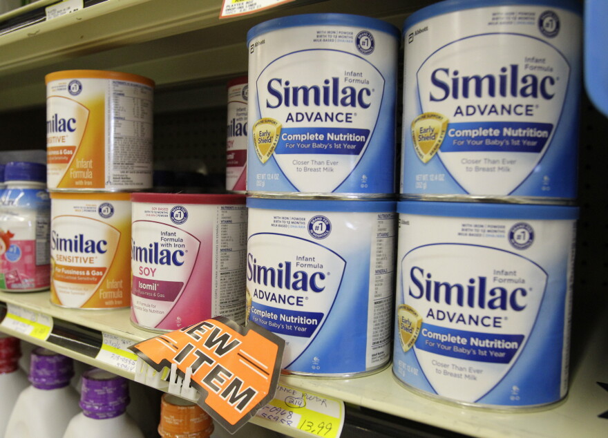 Cans of Similac baby formula sit on a grocery store shelf. The cans are yellow, red and blue. 
