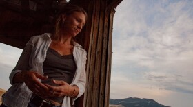 A woman leans against a wooden beam with plains and far away hill in the distance.