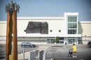 A person walks through an nearly empty parking lot. In the background is a large supermarket building with a black tarp covering the store's name.