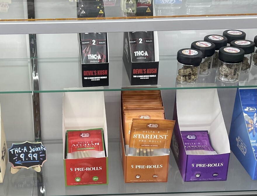Boxes of colorful packages of Delta-8 Pre-Rolls on a glass shelf next to a sign for THC-A joints for $9.99.
