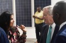 Woman in flower-patterned blouse speaks with two men in suits in front of solar panels