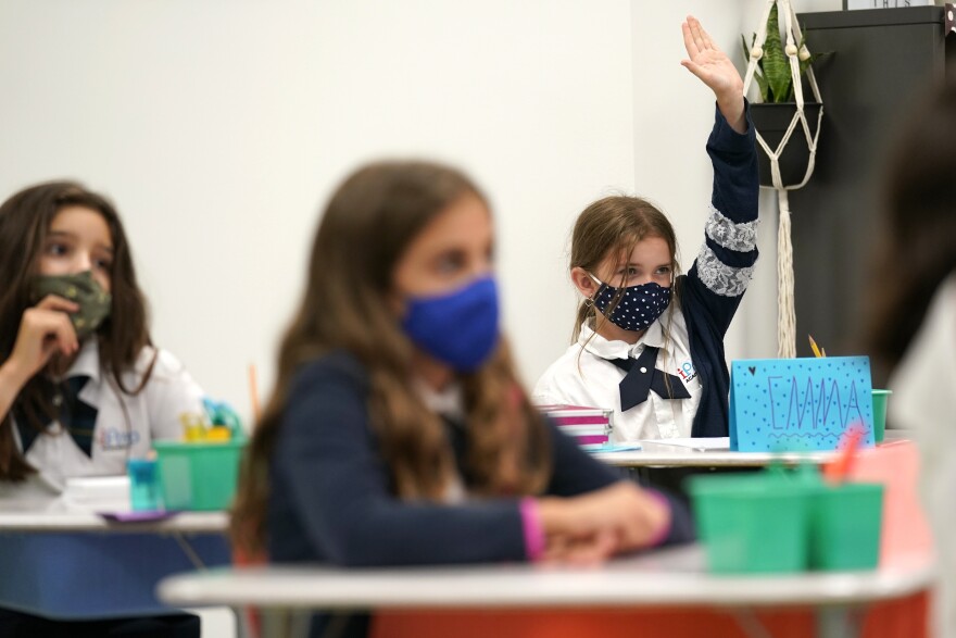 Emma Orell raises her hand in fourth-grade class at iPrep Academy on the first day of school, Monday, Aug. 23, 2021, in Miami. Schools in Miami-Dade County opened Monday with a strict mask mandate to guard against coronavirus infections. 