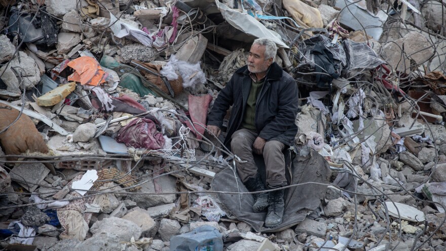 A man watches a search and rescue operation from a pile of rubble in Hatay, Turkey, after the earthquake.