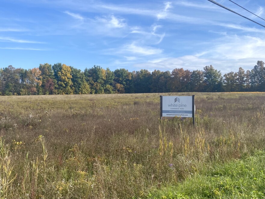 A sign sits in an open field below a blue sky.