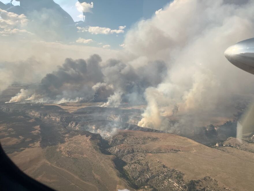 Smoke bellows from multiple points of the prairie near a deep canyon.