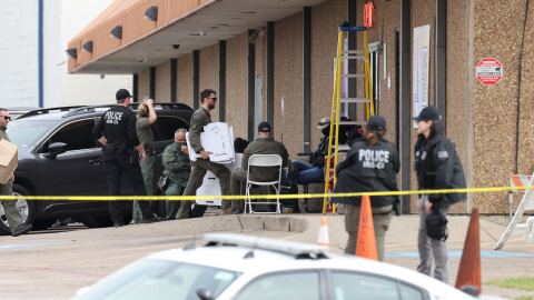 People in law enforcement gather around a storefront behind police caution tape.