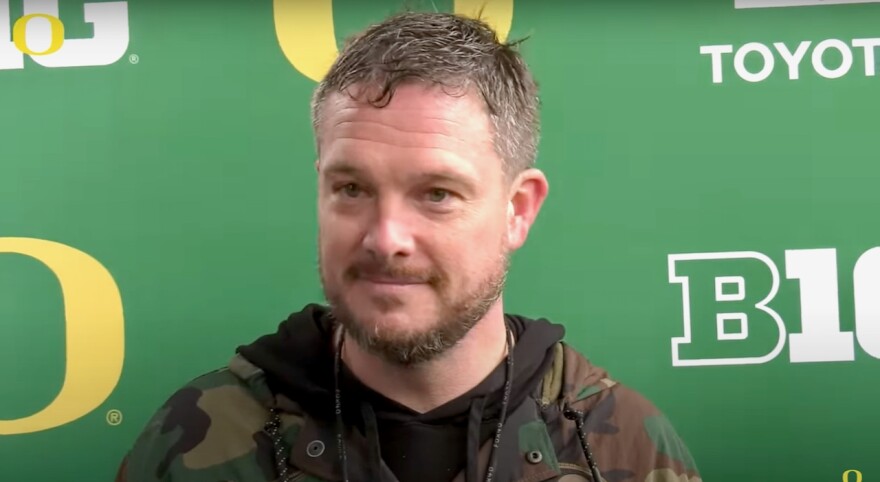Coach Dan Lanning stands in front of a U of O / Big 10 backdrop at a press conference. 