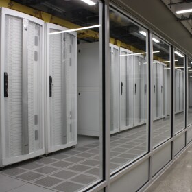 The data center on the third floor of San Pedro I, seen through a wall of glass. White servers are stacked in white metal cages. 