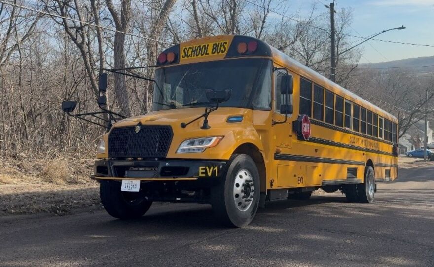 A yellow school bus is climbing a hill. There are many trees without leaves to the left of the bus.
