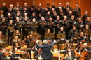 A man in a blue blazer conducts an orchestra