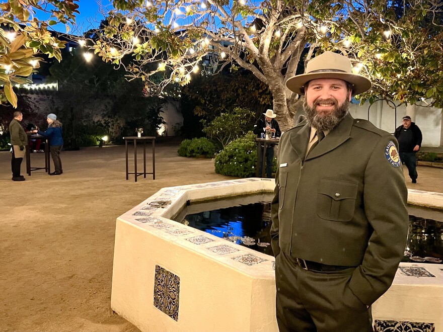 A man in a green state parks uniform smiles and looks at the camera. 