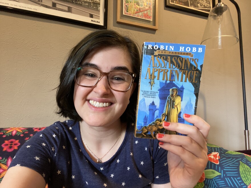 Miranda Suarez sits in her home holding Robin Hobb's 'Assassin's Apprentice'.