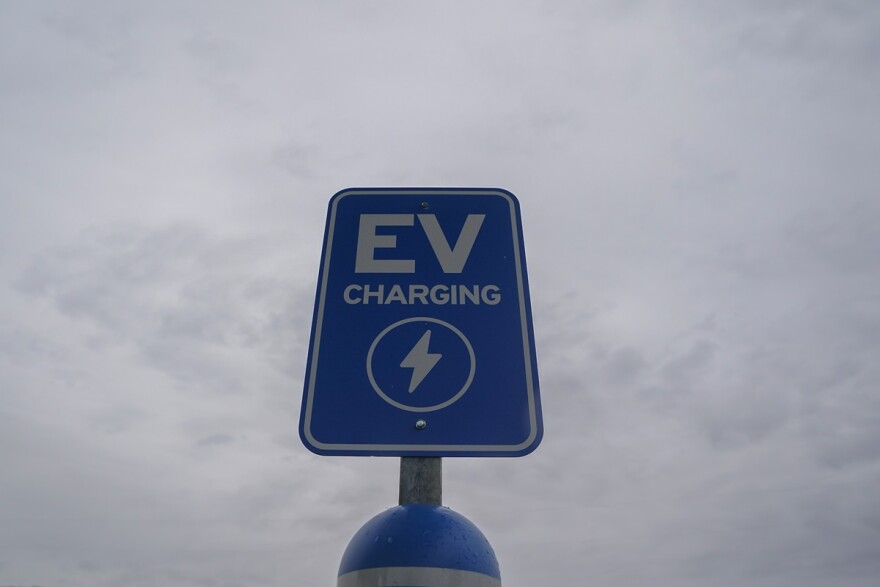 A blue sign with the letters EV charging inscribed and an icon of a lightning bolt below. 