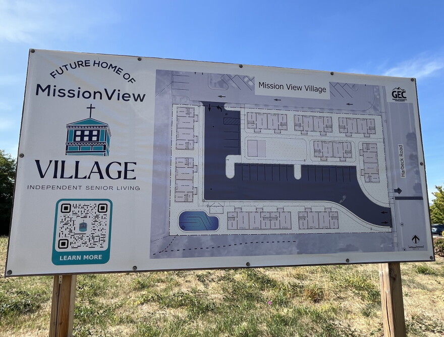 A large sign posted in a grass lot shows a purple architectural layout plan for the site. 