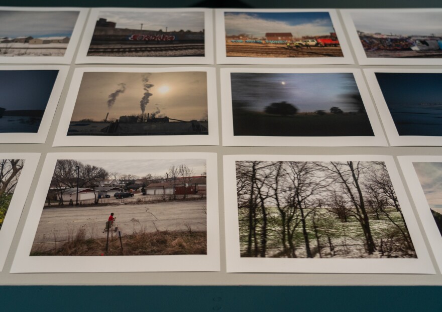 Three rows of photos in muted tones are lined up on a table. They show images of graffiti, a factory, trees and a child riding a bicycle, slightly blurred from being shot while on a train.