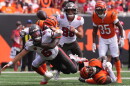 football player in white jersey and pewter helmet is tackled and watches the ball leaves his hands and is in the air. behind him is another player who made the tackle in an orange jersey and helmet on the ground, and two other players running from behind them