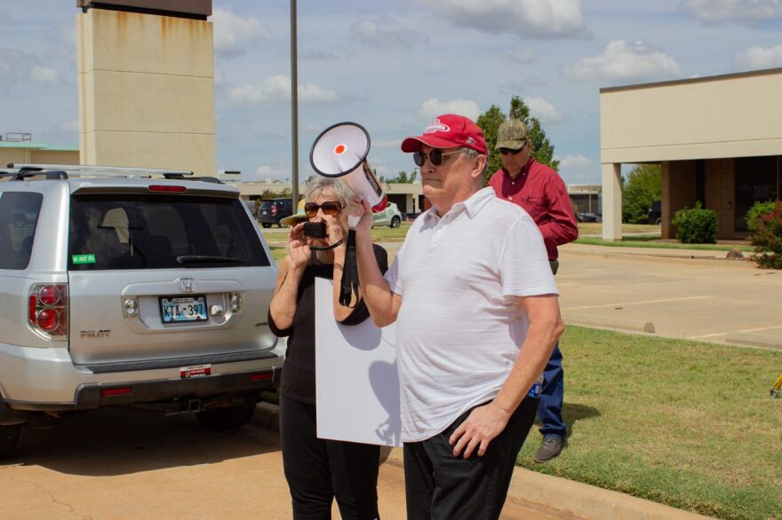 A Pike Off demonstrator speaks through a bullhorn aimed at building housing the fundraiser. “I would just like to say,” she said. “A man of integrity would walk out here, walk on those steps, come down on the grass knoll and say, ‘I want to talk to you.’”