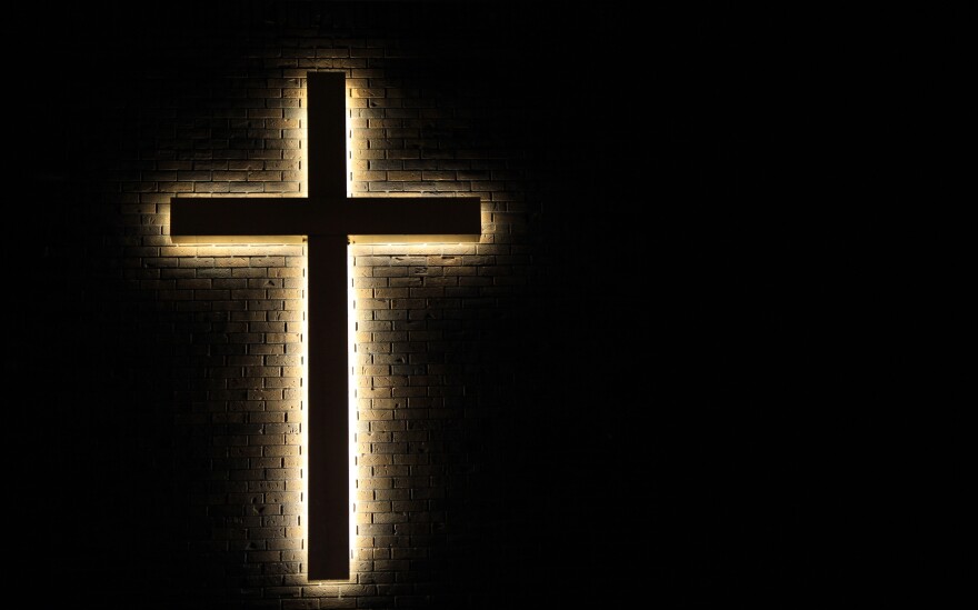 religious cross hanging on side of building with lights behind it