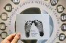 A hand is shown holding up a piece of paper showing baby ink footprints.