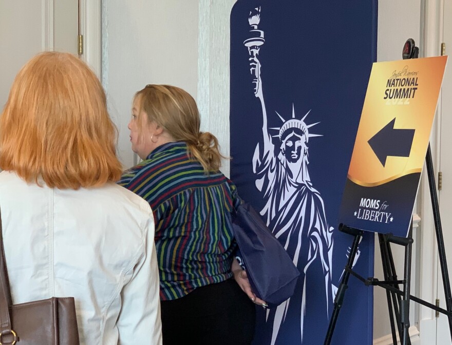 Two women walk into a conference room next to a picture of the statue of liberty