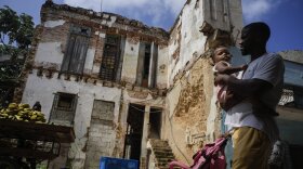 Man holds child while walking past crumbling building