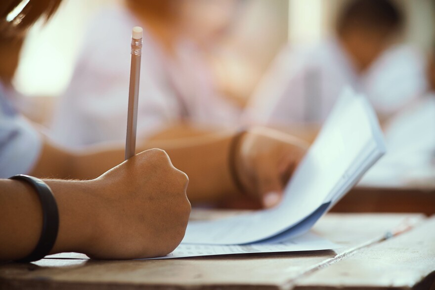 This stock image shows a student holding a pencil and taking an examination.