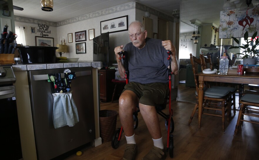 An elderly man in a wheelchair inside his kitchen. 