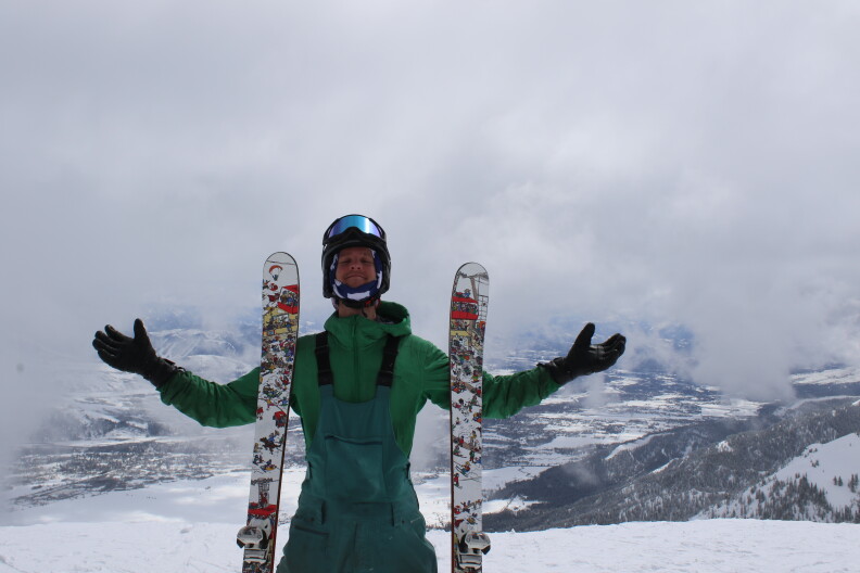 A person in ski gear poses with their skis at the top of a mountain.