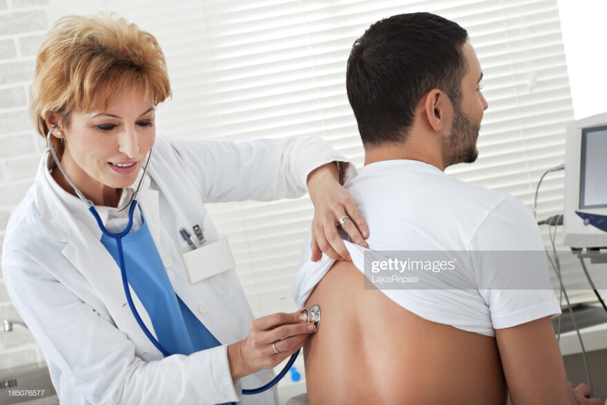 Female doctor examining a young man - by Lajos Repasi