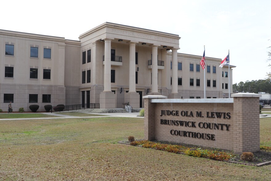 The Brunswick County Courthouse, a large tan building with four pillars, on a cloudy day. 