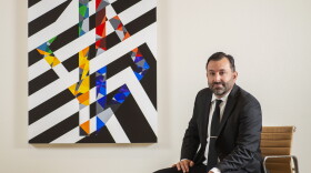 Scott Malbaurn sits beside a geometric painting with black-and-white stripes and colorful triangles.