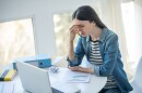 An upset woman sits at her desk with a laptop and an unemployment claim, face in her hand