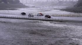 Vehicles cross over a flood control basin that has almost reached the street, Sunday, Aug. 20, 2023, in Palm Desert, Calif.