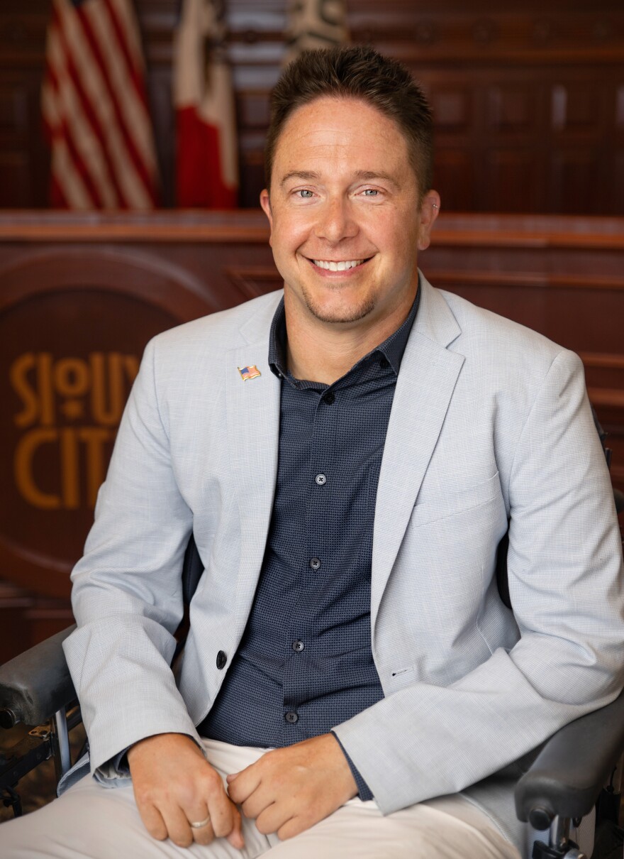 a smiling man wearing a jacket with an American flag pin on the lapel