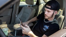Cameron Basden places sports bets from his phone on Monday, Aug. 28, 2023, in the parking lot of a TJ Maxx in Fairview Heights, Ill. Basden is a resident of Mehlville, Mo., but drives across the river to Illinois on a regular basis to bet on sports. The betting is his main source of income. 