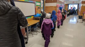A line of elementary children line up and walk down the hallway out to recess in the winter