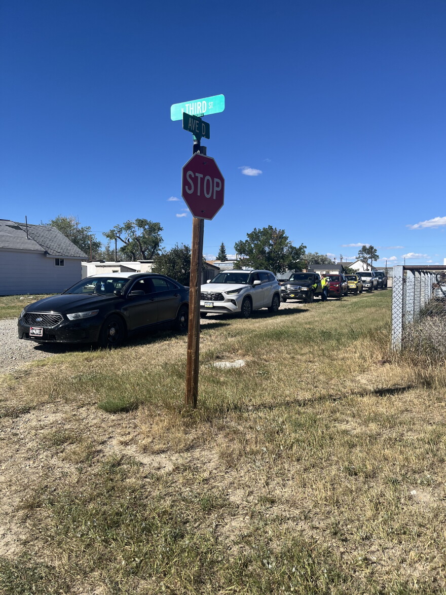 A line of cars waiting to receive food in Rock River. A stop sign in the foreground.