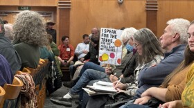 A Logan resident holds a sign in a crowded City Hall that reads "I speak for the trees, for the trees have no tongues."