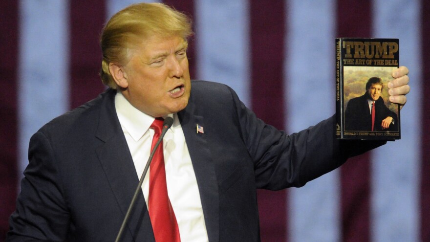 Candidate Trump holds up his book "The Art of the Deal," given to him by a fan in Birmingham, Ala. In the book, he espouses "truthful hyperbole."