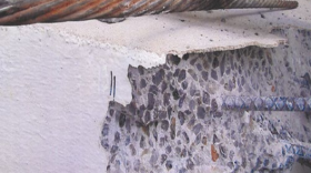 A close-up on corrosion of a structural element to a condo building. Sections of concrete have broken away, reveling metal bars.