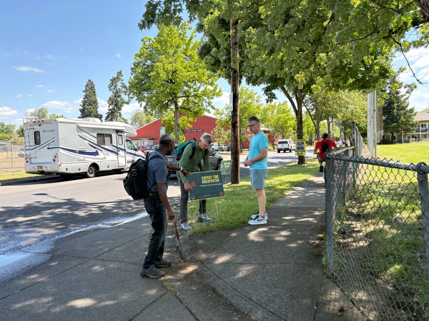 Community members from various groups plant signs on the stretch of road where a University of Oregon doctoral student was killed on May 27, 2026