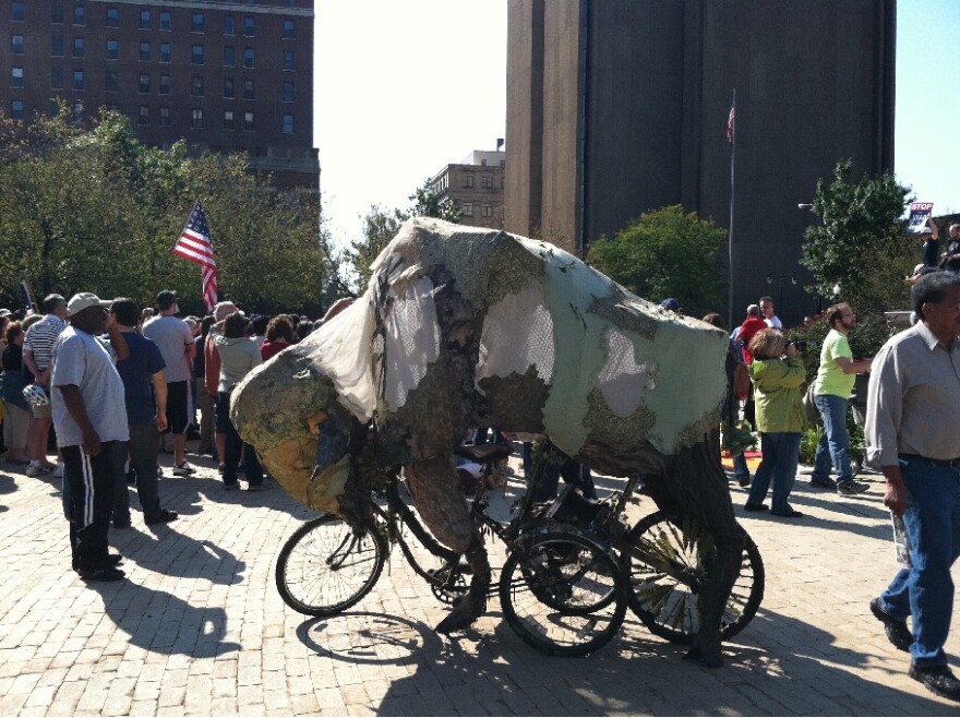 Protestor Frank Levoy rode his bicycle - modified to look like a buffalo dressed in camouflage - around the perimeter of Saturday's event, while wearing a deer skin cap.